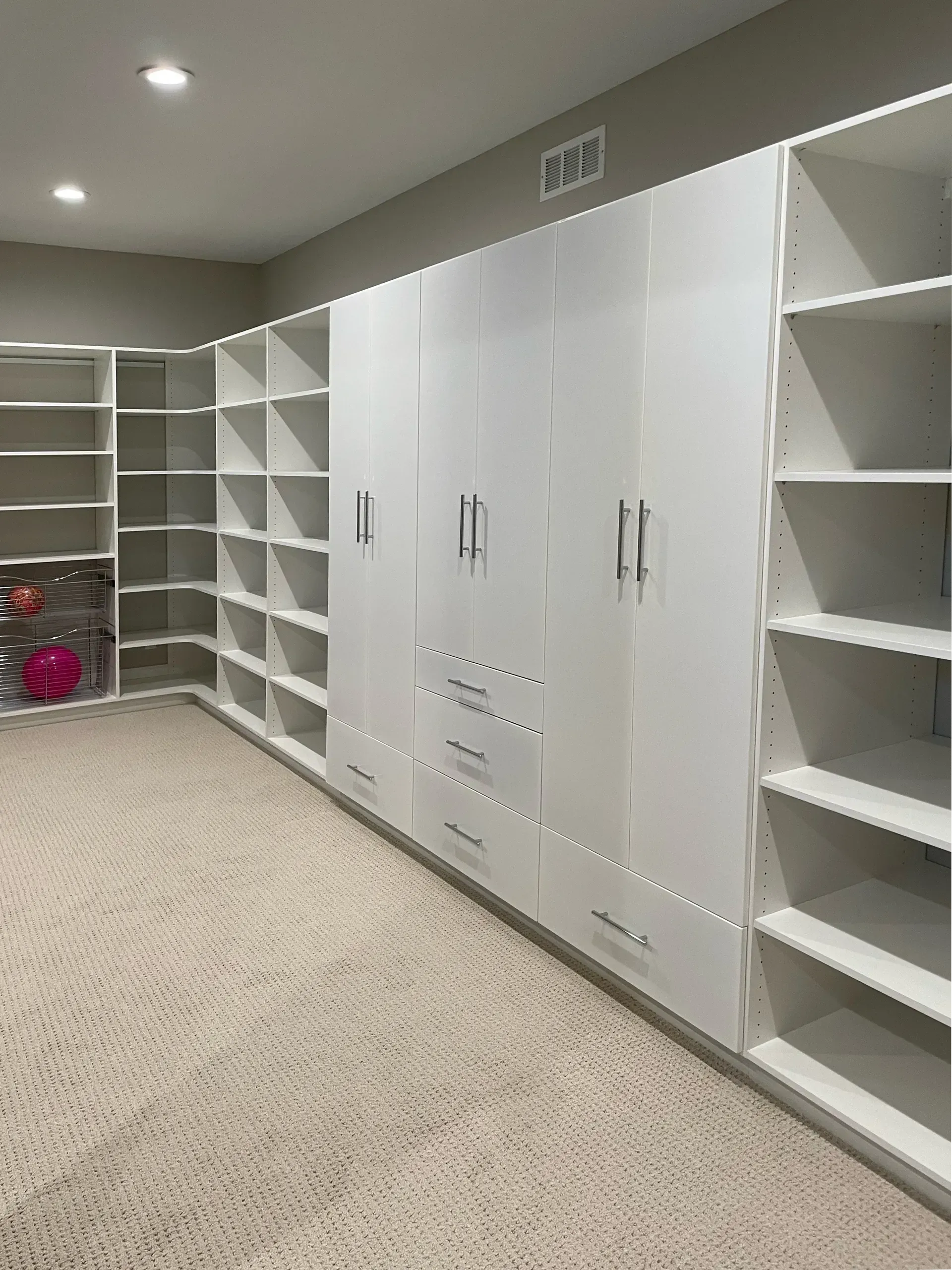 White built-in closet with shelves, drawers, and cabinets on beige carpet.