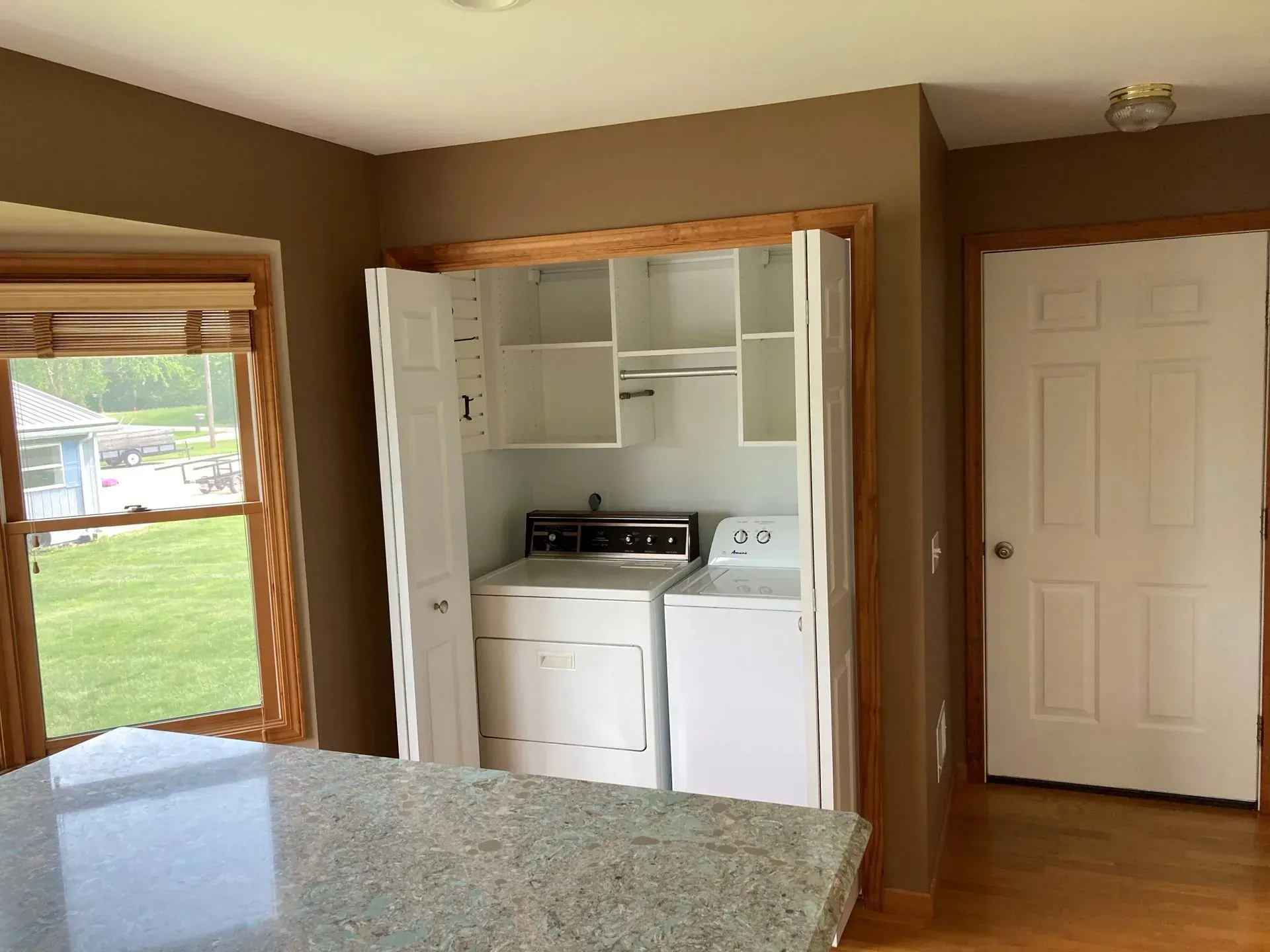 Laundry machines in a white cabinet, near a window and a door.