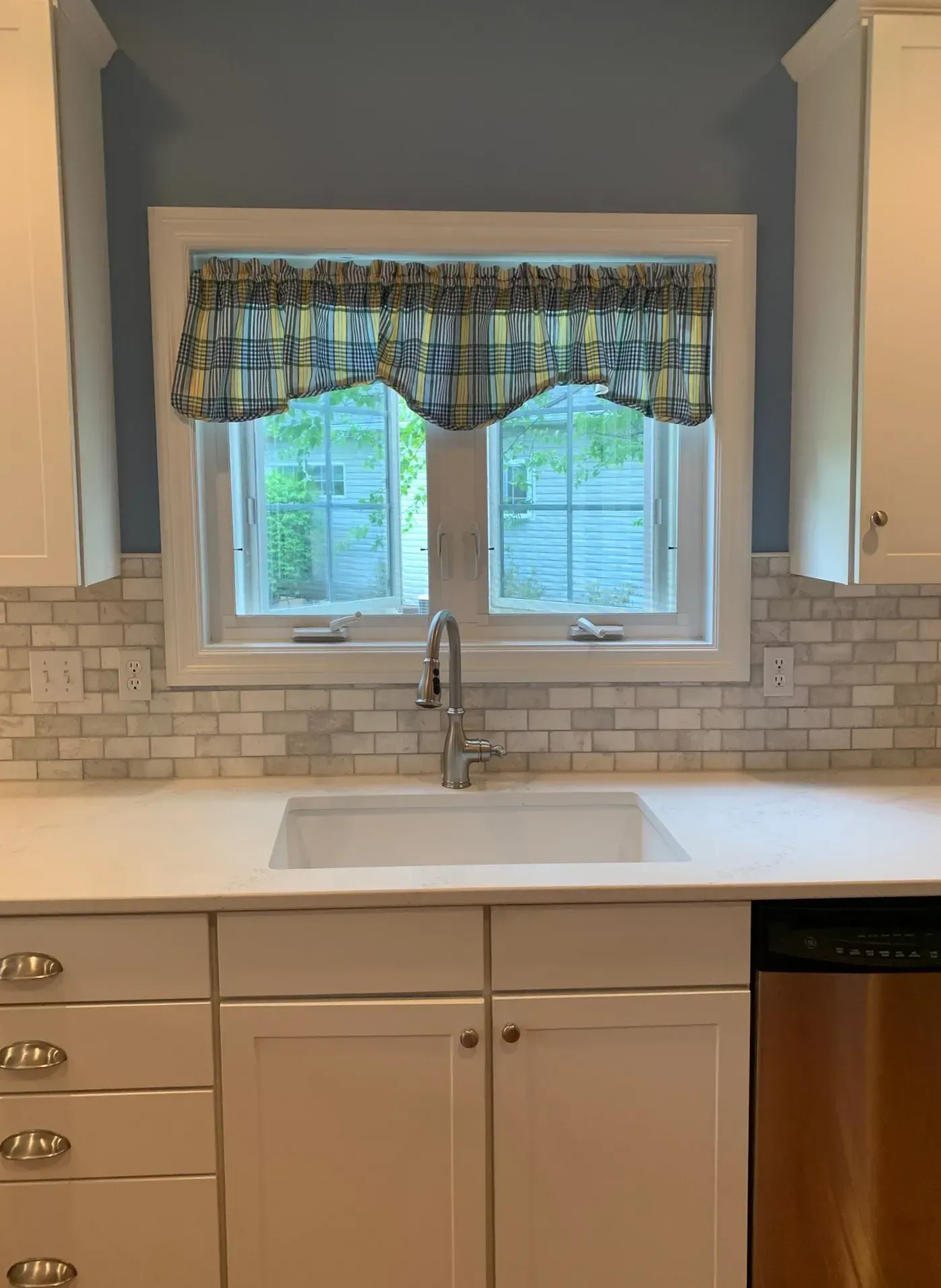 Kitchen with white cabinets, a sink, and window with blue plaid valance.