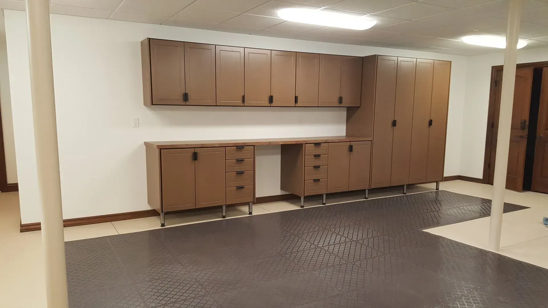 Brown cabinets and desk against a white wall in a basement with dark gray flooring.