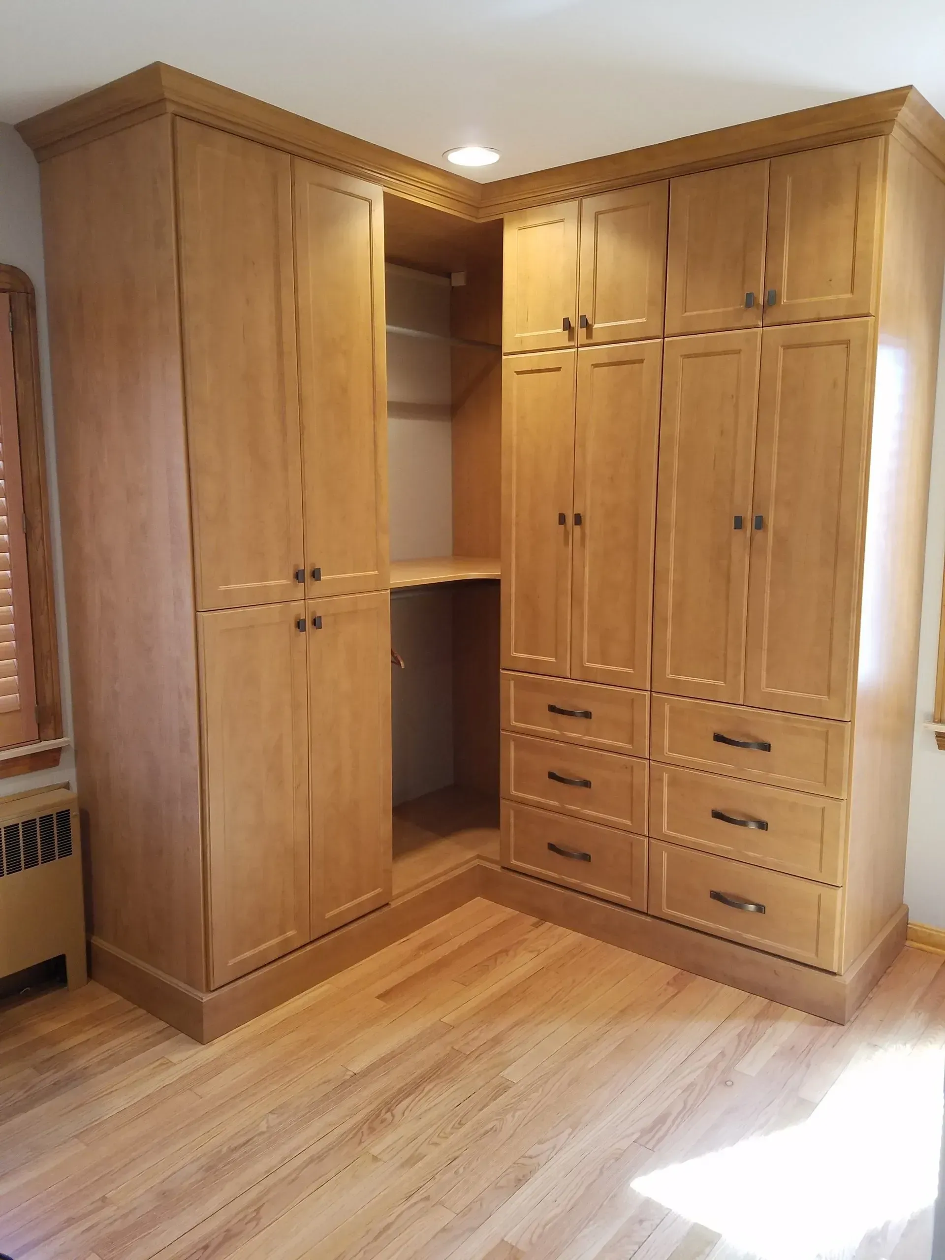 Corner wooden cabinets with drawers and doors in a room with hardwood floors.