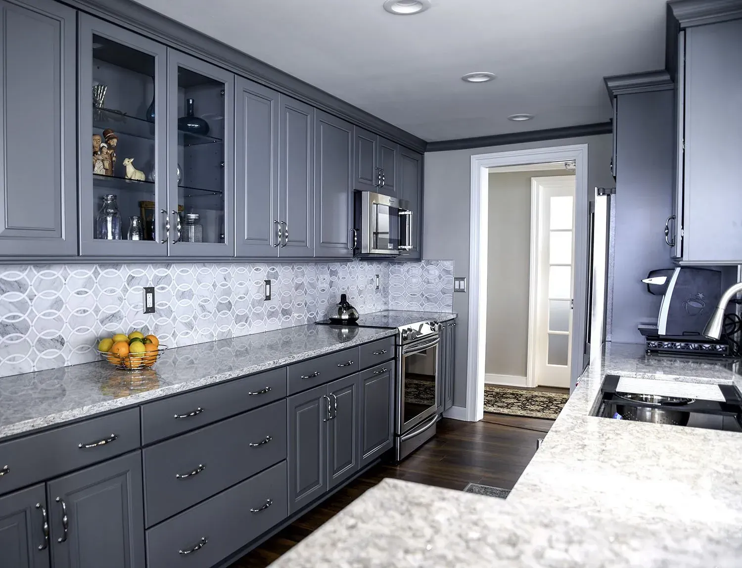 Gray kitchen with granite countertops, stainless steel appliances, and a doorway leading to another room.