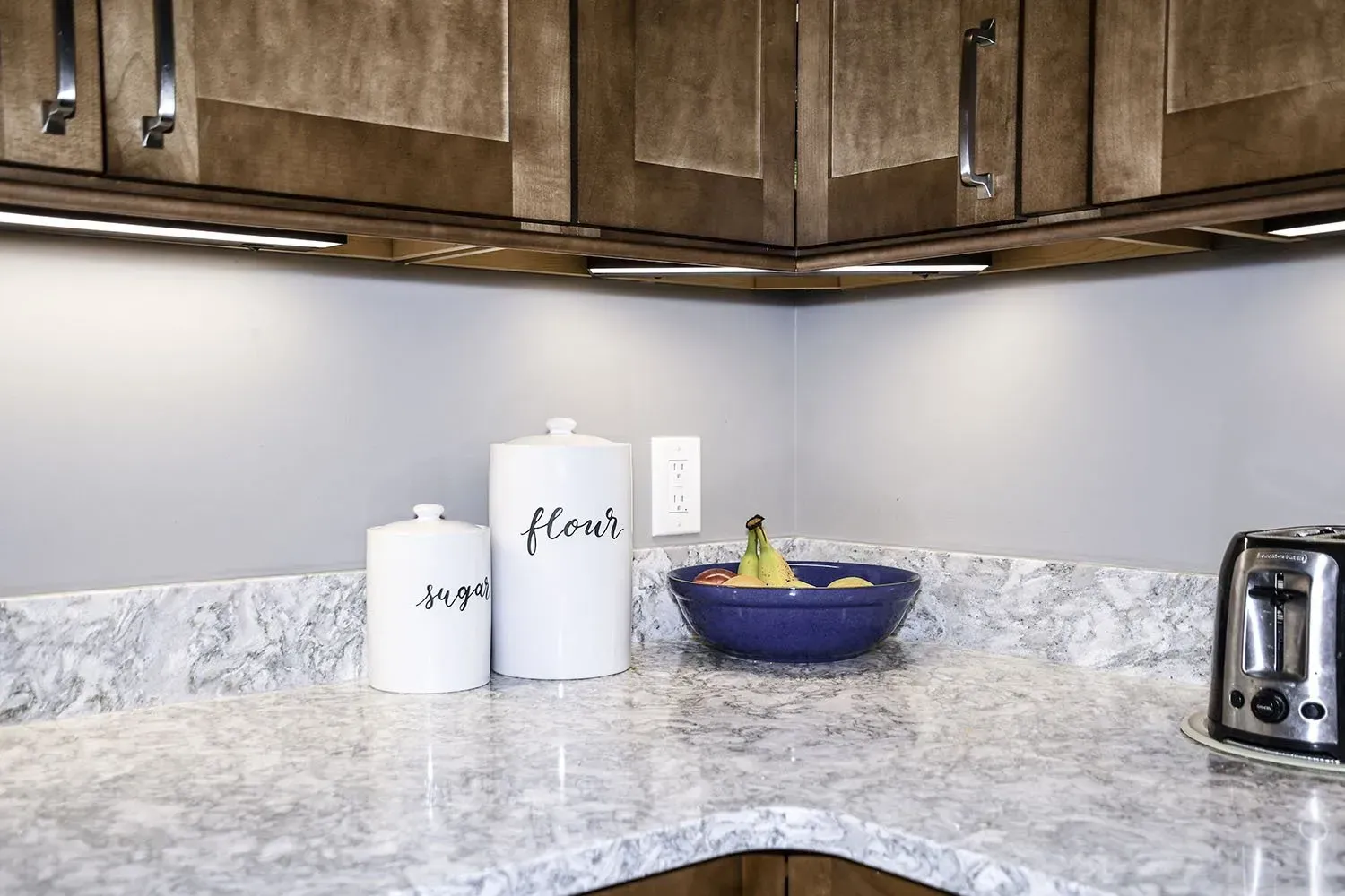 Kitchen countertop with sugar and flour canisters, a bowl of fruit, and a toaster.