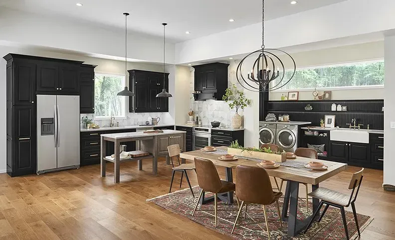Modern kitchen with black cabinets, wood floor, large island, and dining table.