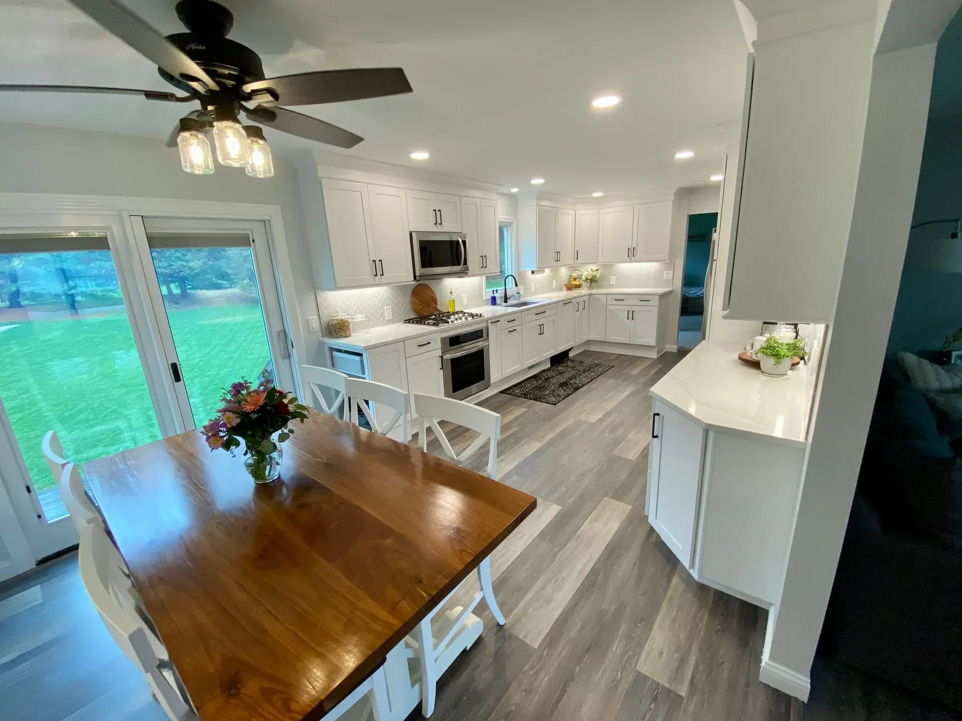 Bright, modern kitchen with white cabinets, dark wood table, and gray floors; a view into a grassy backyard.