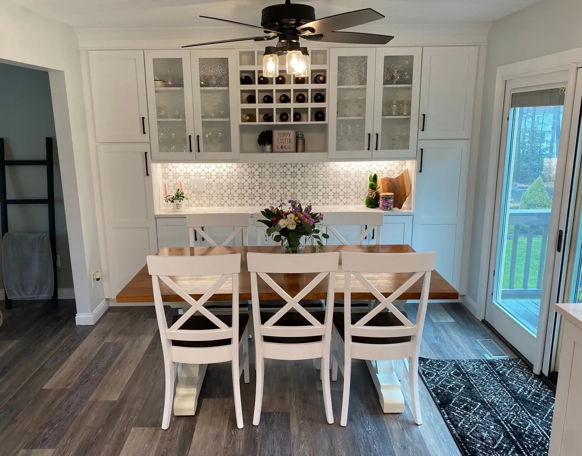 White kitchen with cabinets, wine rack, table, chairs, and open doors to a deck.
