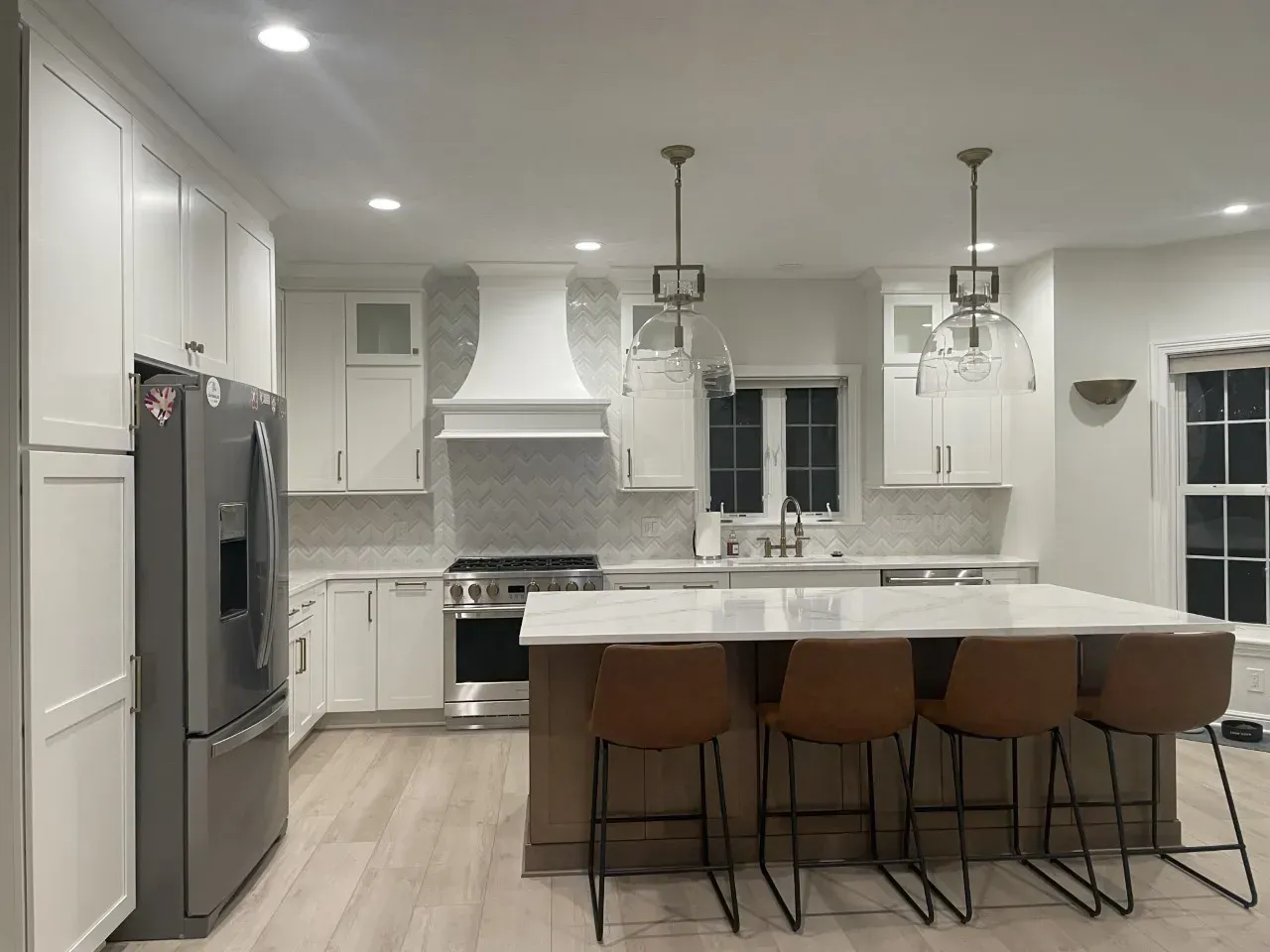 Modern white kitchen with stainless steel appliances, a large island, and brown leather bar stools.