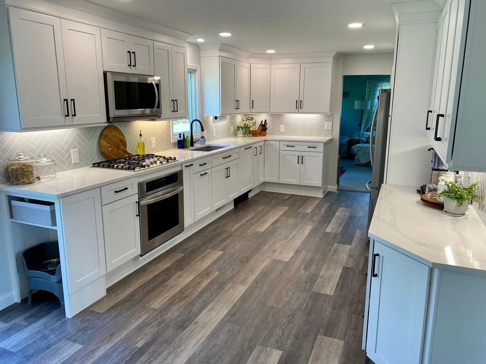 White kitchen with wood-look flooring, white cabinets with black hardware, and stainless steel appliances.