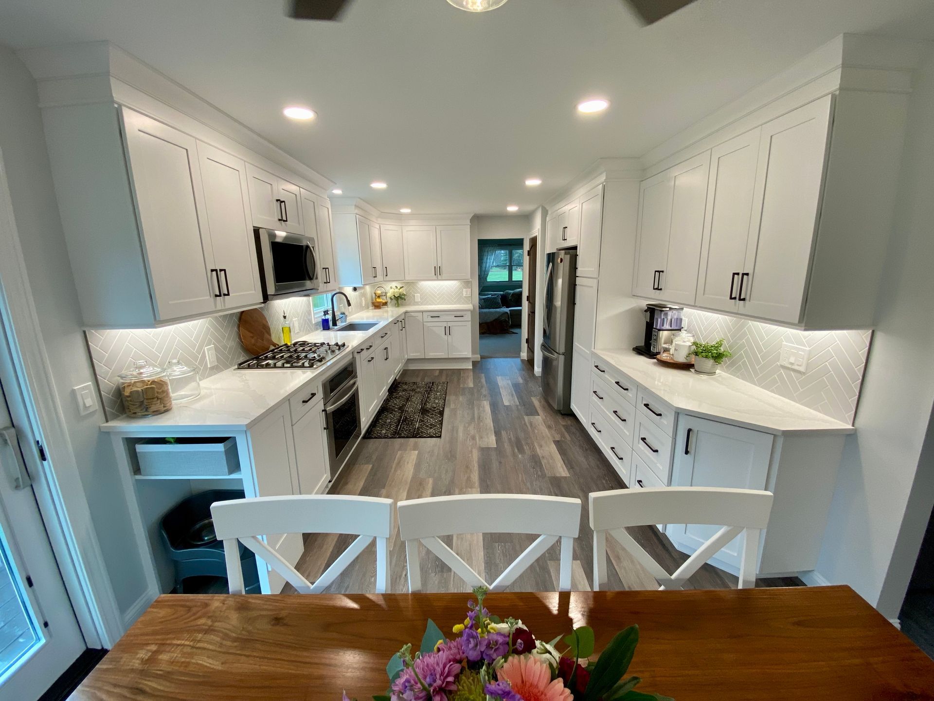 Bright, modern kitchen with white cabinets, countertops, and wooden dining table.