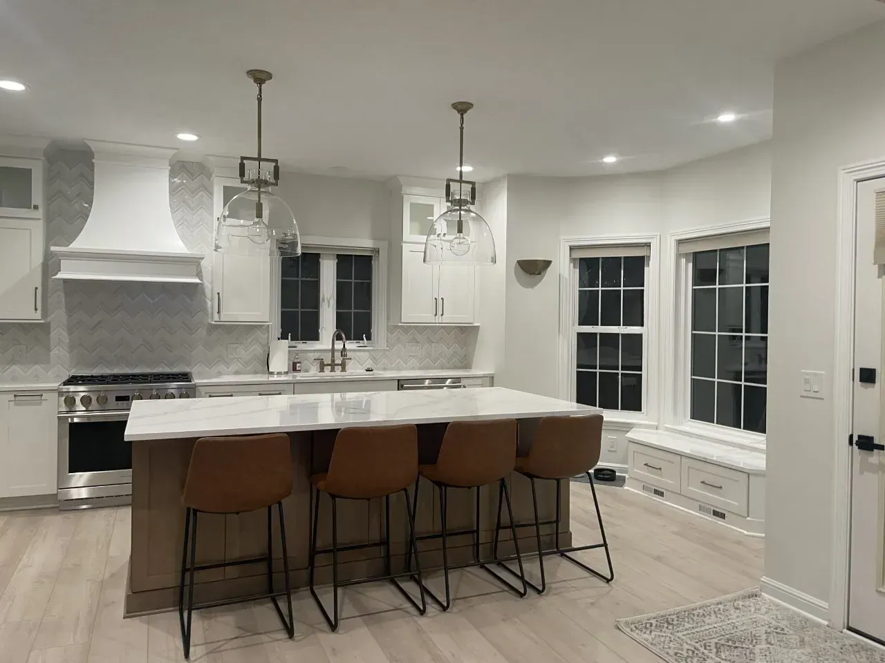 Modern white kitchen with a large island and brown bar stools.