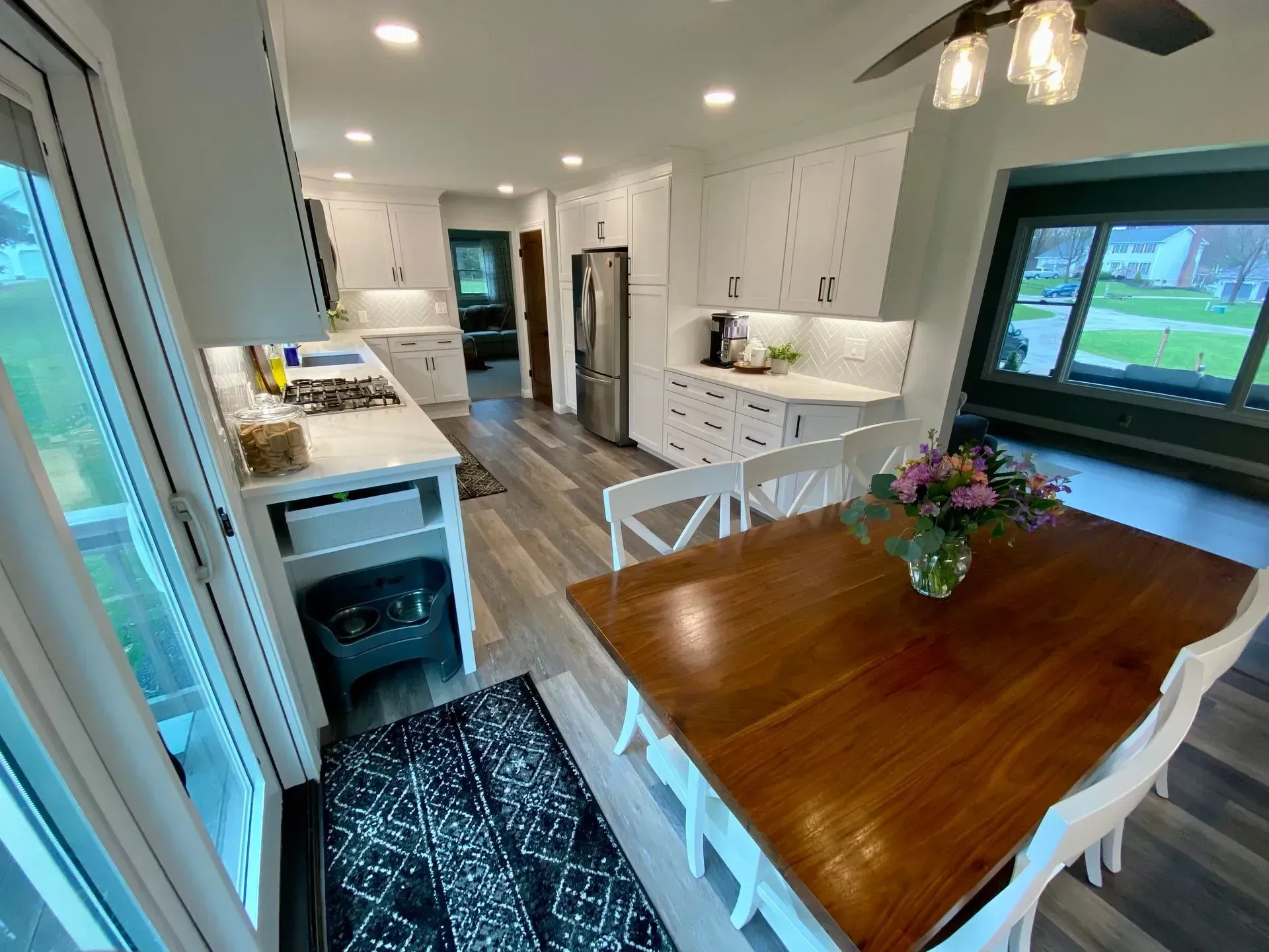 Bright white kitchen with a wooden table, white chairs, and a dark rug.