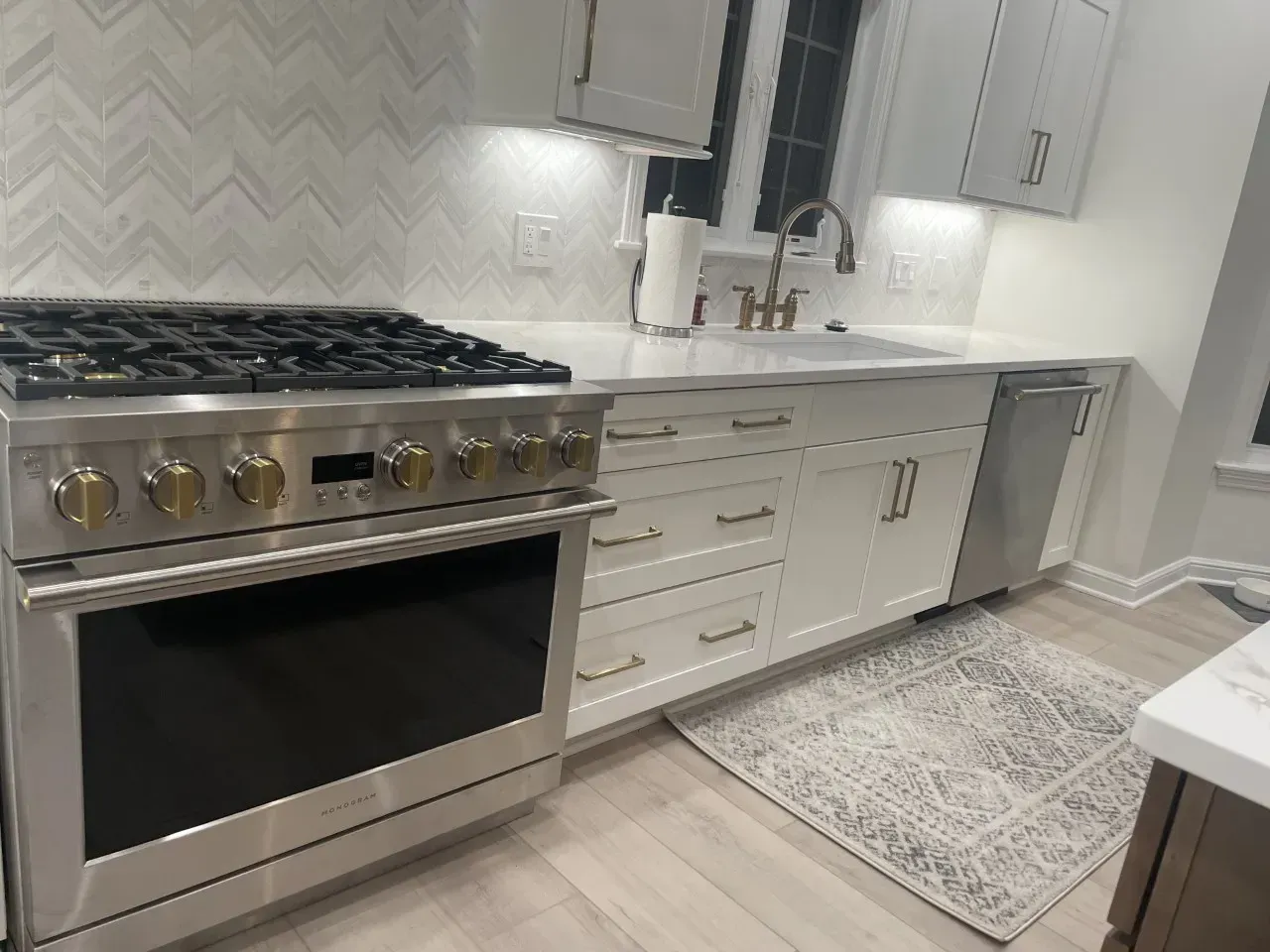 Modern kitchen with stainless steel range, white cabinets, and a gray rug.