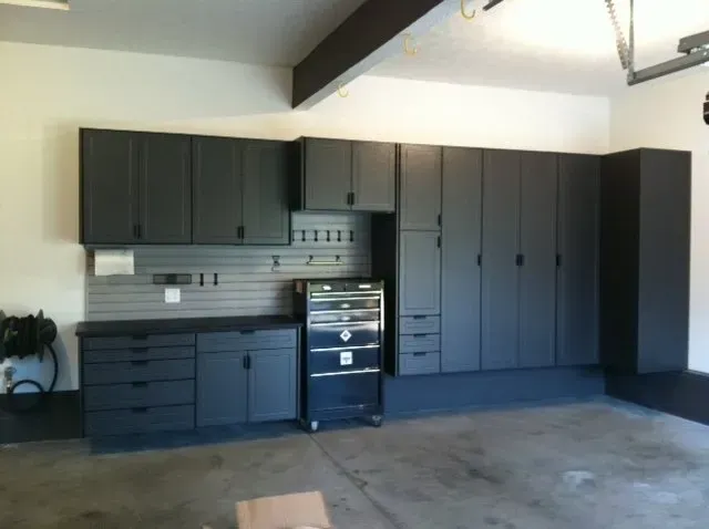 Garage with dark gray cabinets, tool chest, and pegboard; white walls and concrete floor.
