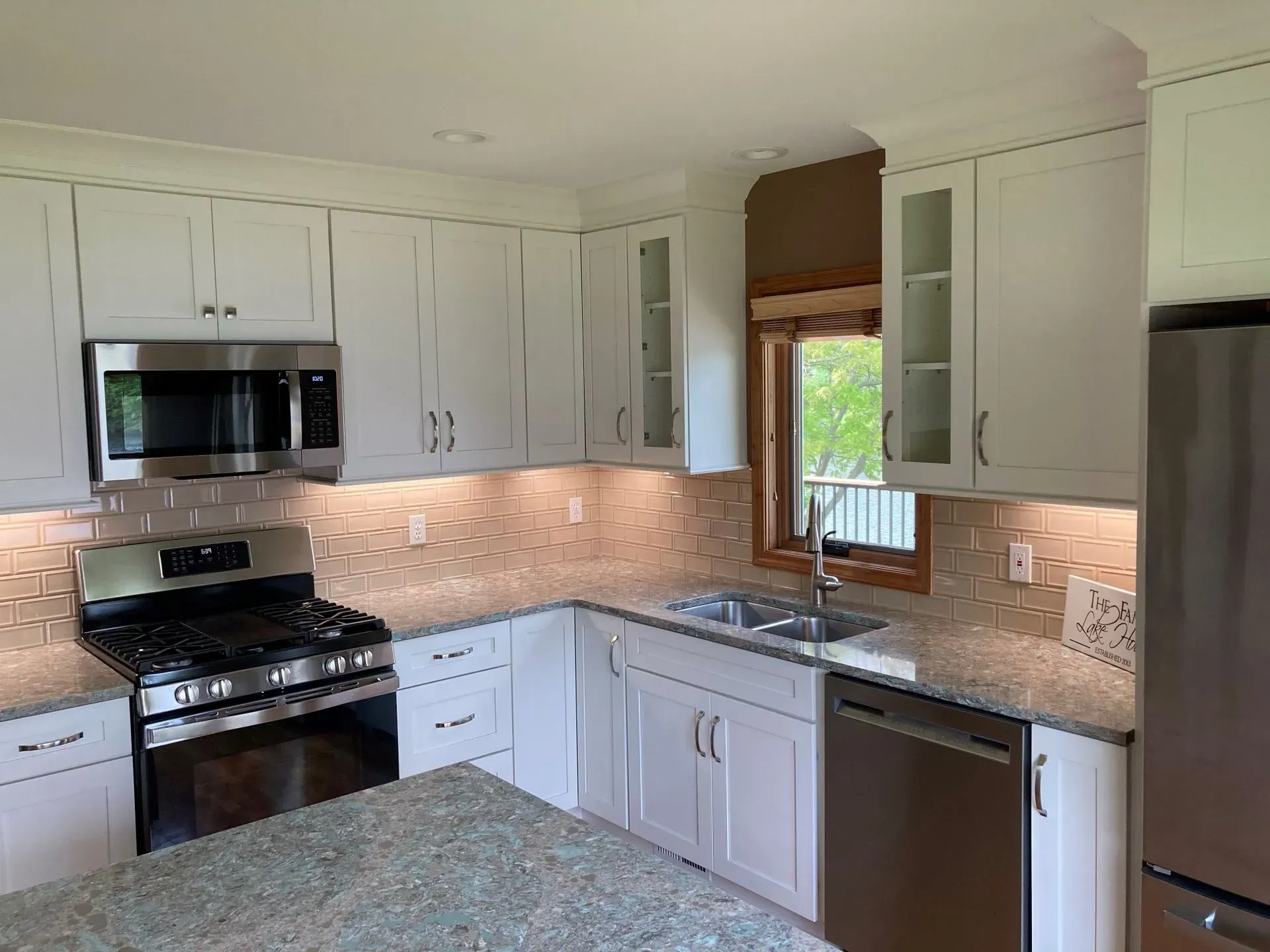 White kitchen with stainless steel appliances, light granite countertops, and a window.