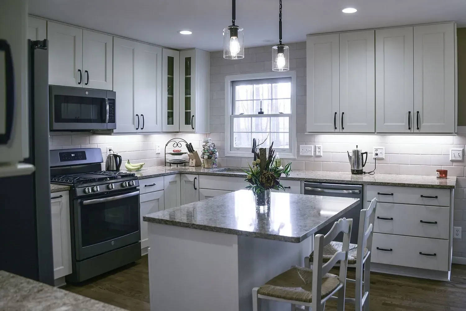 White kitchen with island, stainless steel appliances, granite countertops, and pendant lights.