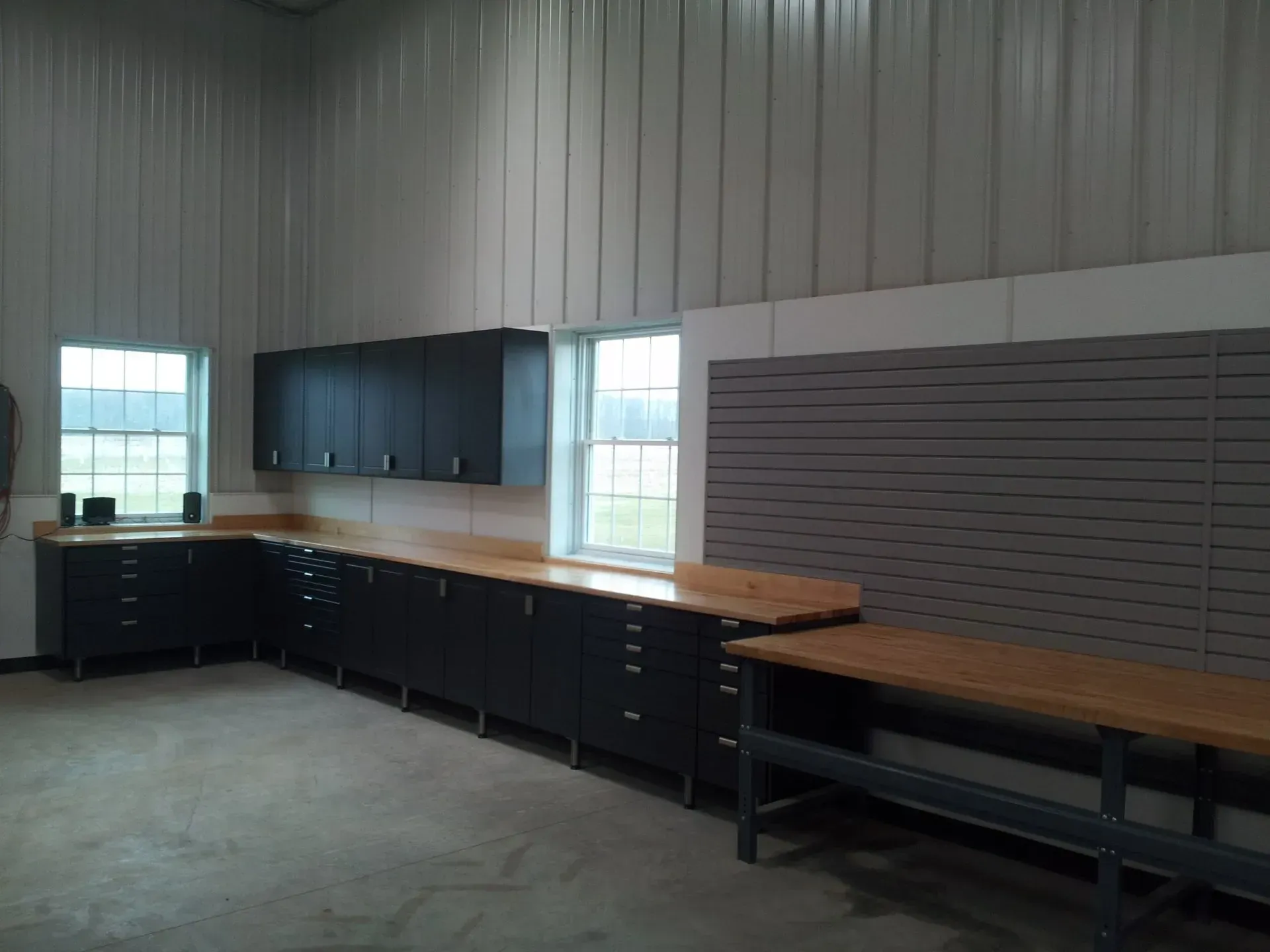 Workshop with dark cabinets, wood countertops, and pegboard against a metal wall.