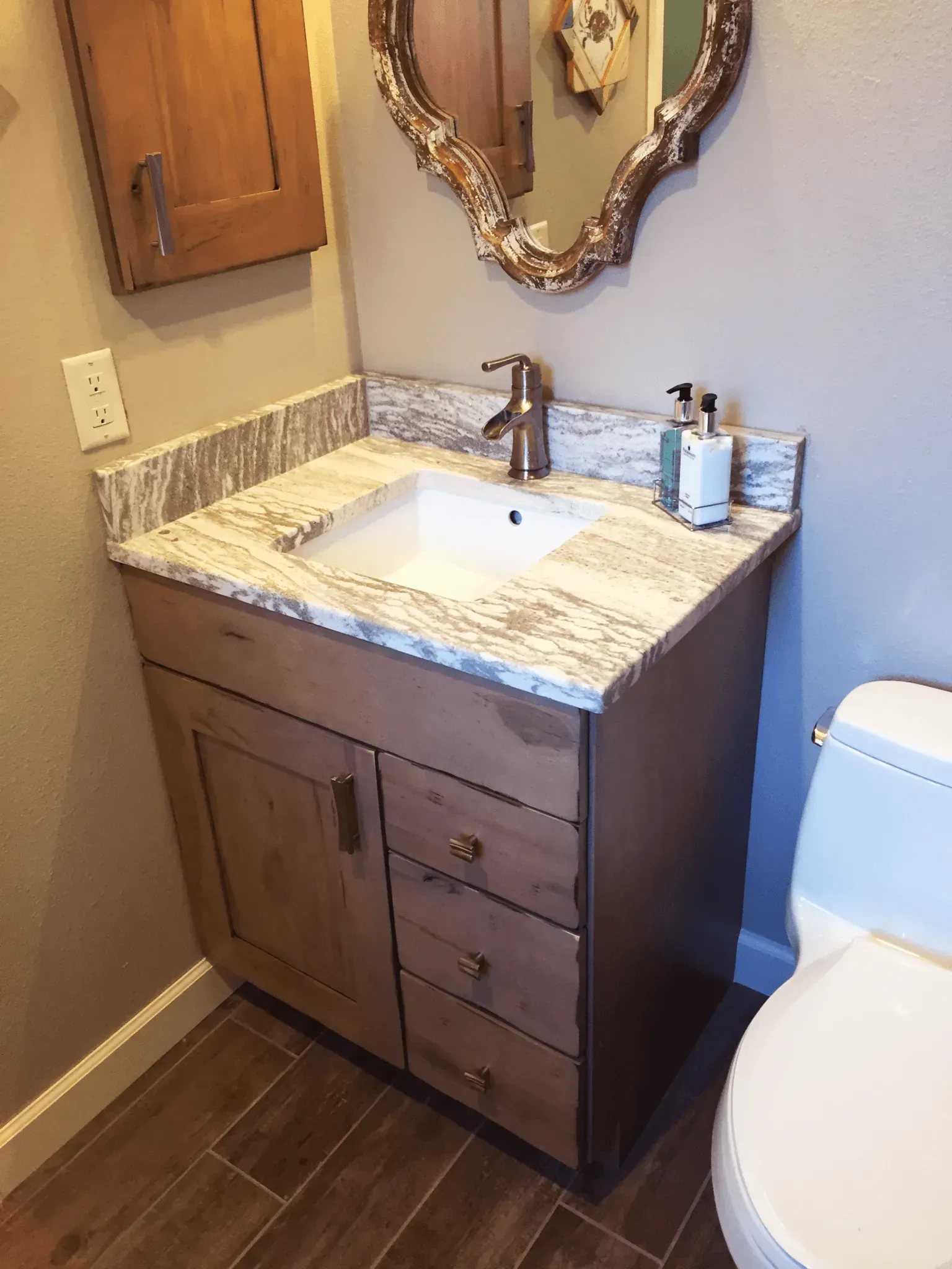 Bathroom with wooden vanity, marble countertop, sink, gold faucet, and decorative mirror.