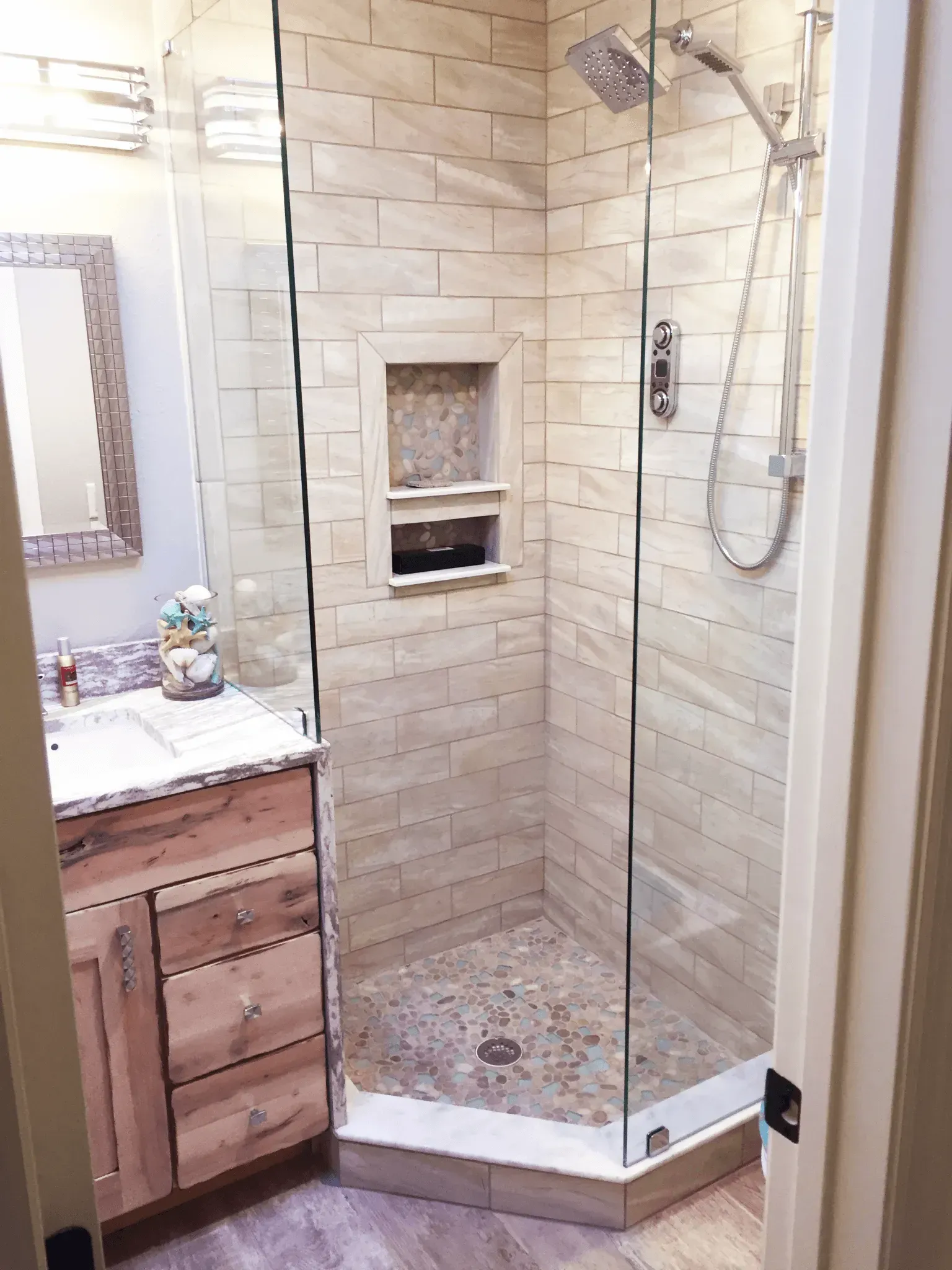 A small bathroom with a glass shower, wooden vanity, and beige tile walls.