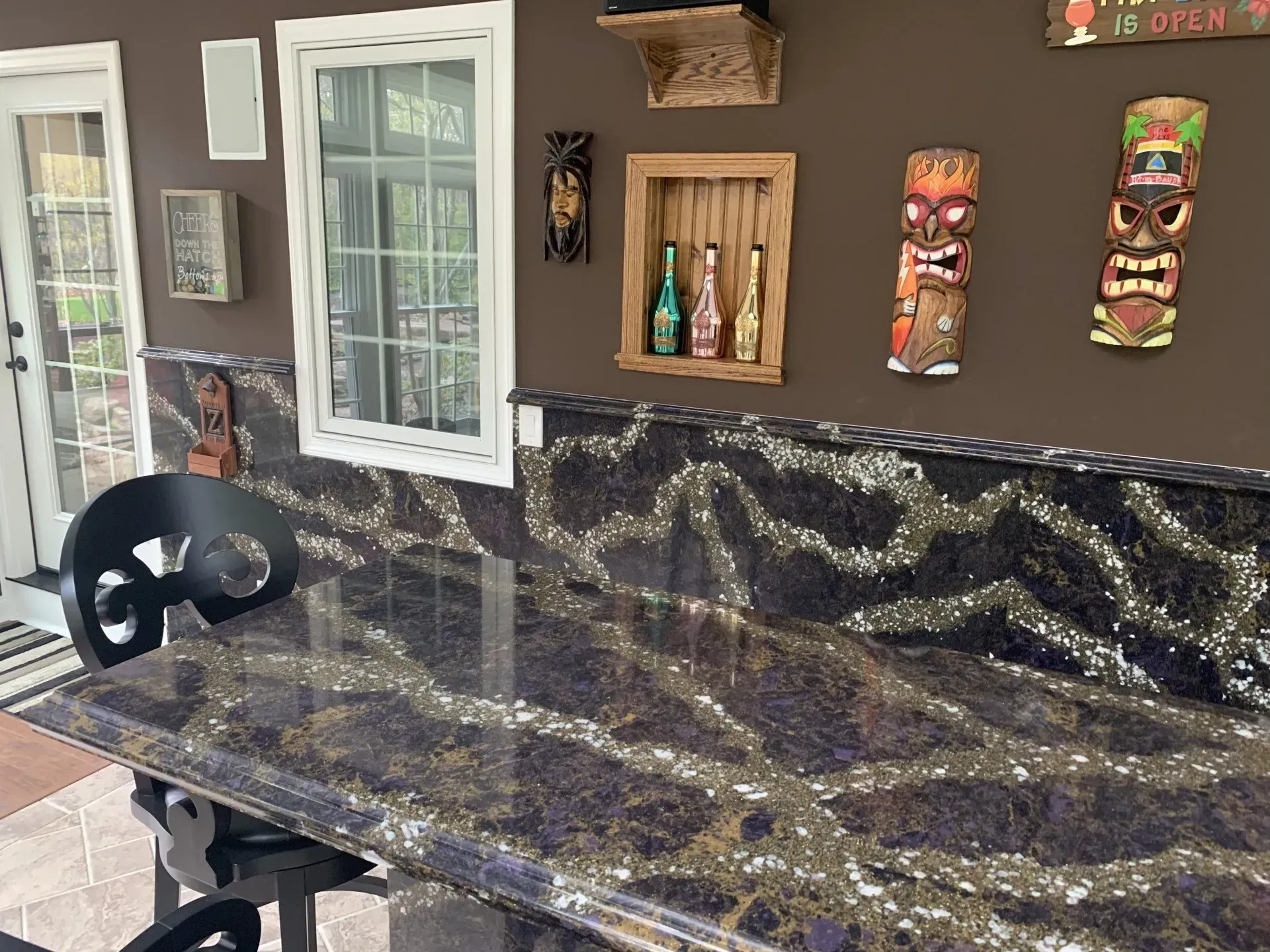 Bar with dark countertop and tiki decorations on a brown wall.