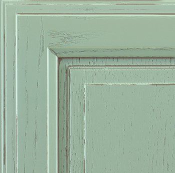 Close-up of a distressed, mint-green cabinet door with raised paneling and visible wood grain.