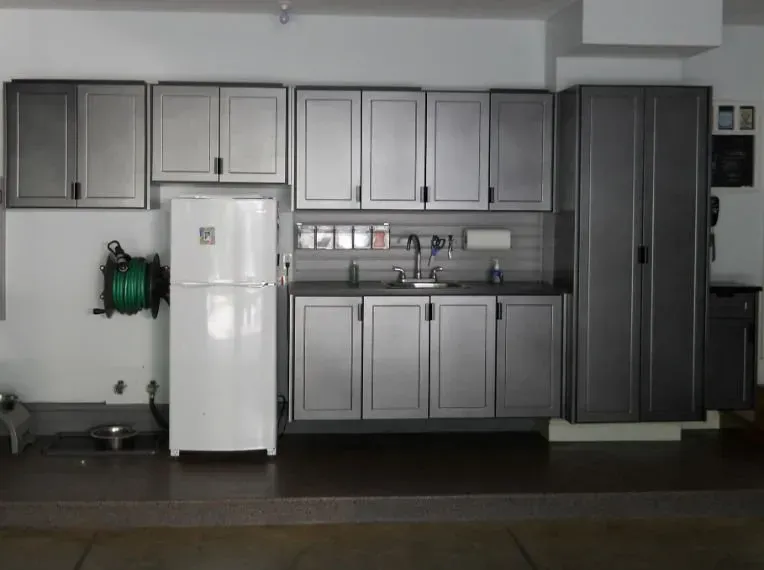 Garage kitchen with gray cabinets, white refrigerator, sink, and hose reel.
