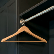 Wooden clothes hanger hanging from a metal rod in a dark closet.