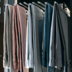 Pants of various colors, hanging from a pull-out rack inside a closet.