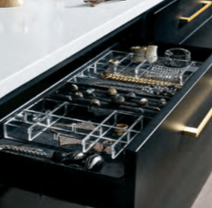 A drawer with clear acrylic jewelry organizers, holding necklaces, rings, and bracelets, on a black cabinet.