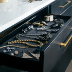 Black drawer holding jewelry, gold handles, white countertop, gray velvet lining.