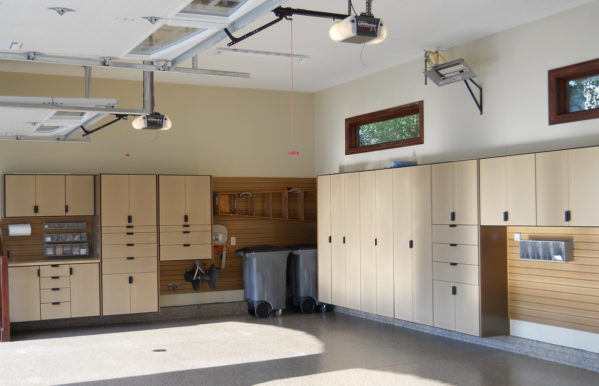 Well-organized garage with tan cabinets, pegboards, and two garage door openers.