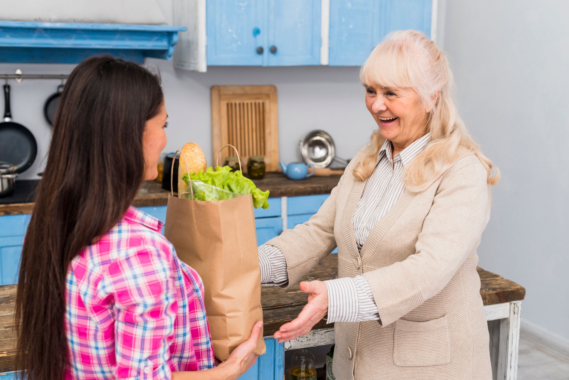 Une femme donne un sac de courses à une femme plus âgée dans une cuisine.