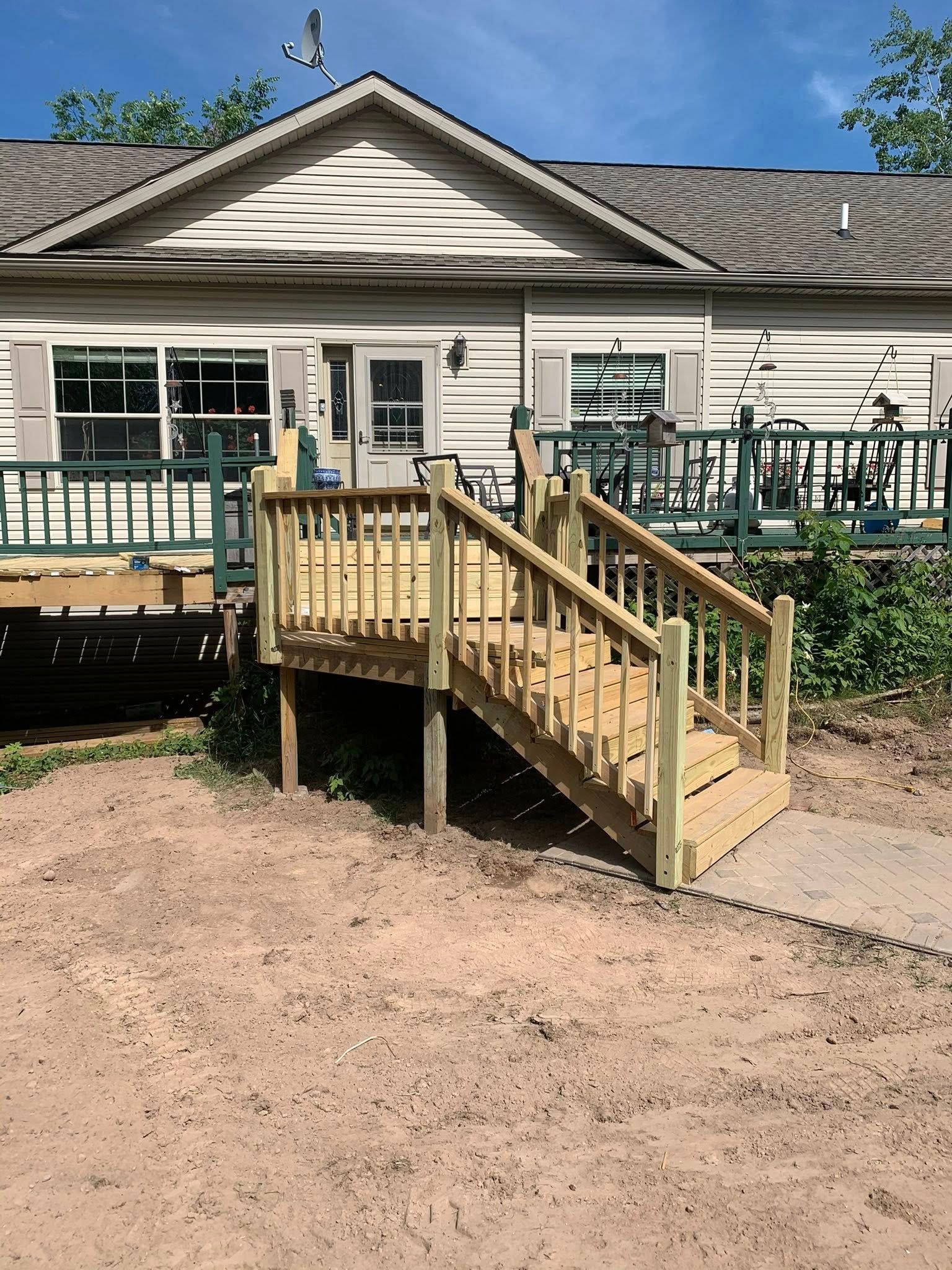 Newly built wooden stairs with a railing leading from a dirt yard up to a house deck.