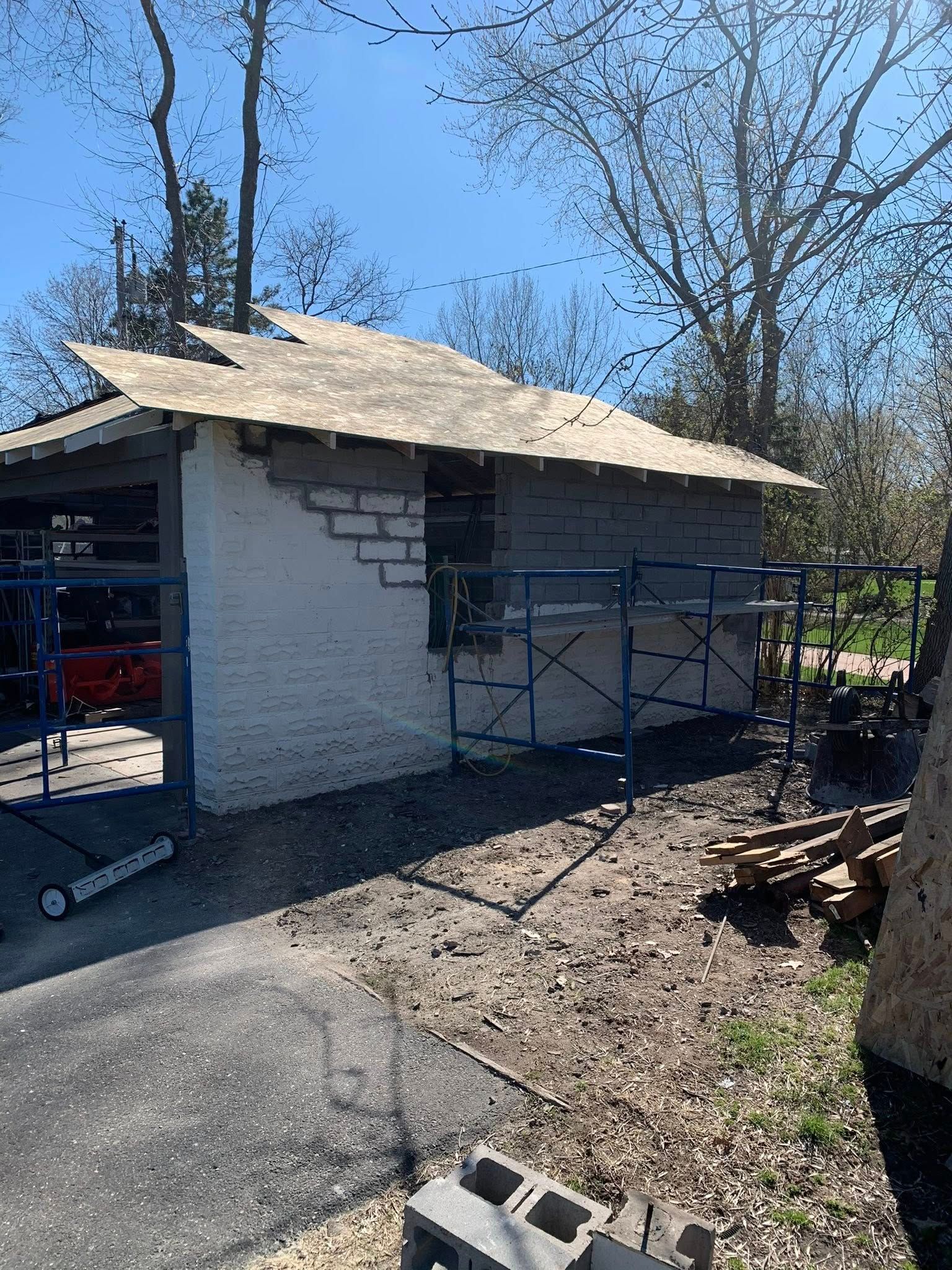 A partially renovated detached garage with a new plywood roof and exterior concrete block walls under repair.