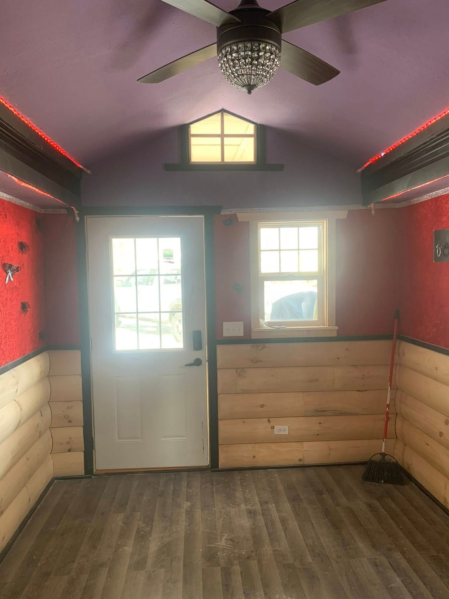 Small room with purple ceiling, red walls, log-style wooden lower walls, wood-look floor, and a central ceiling fan.