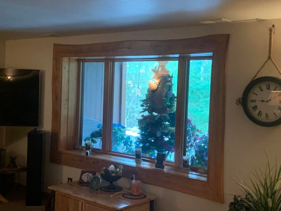 A rectangular window with a wide, natural-edge wood frame, displaying an outdoor view with a small decorated tree.