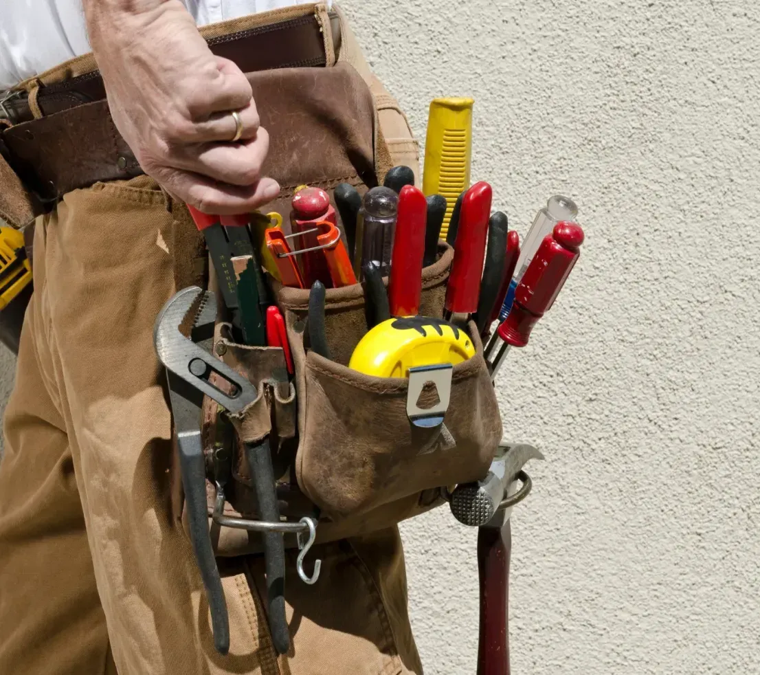 A person wearing a brown leather tool belt filled with various pliers, screwdrivers, and a hammer.