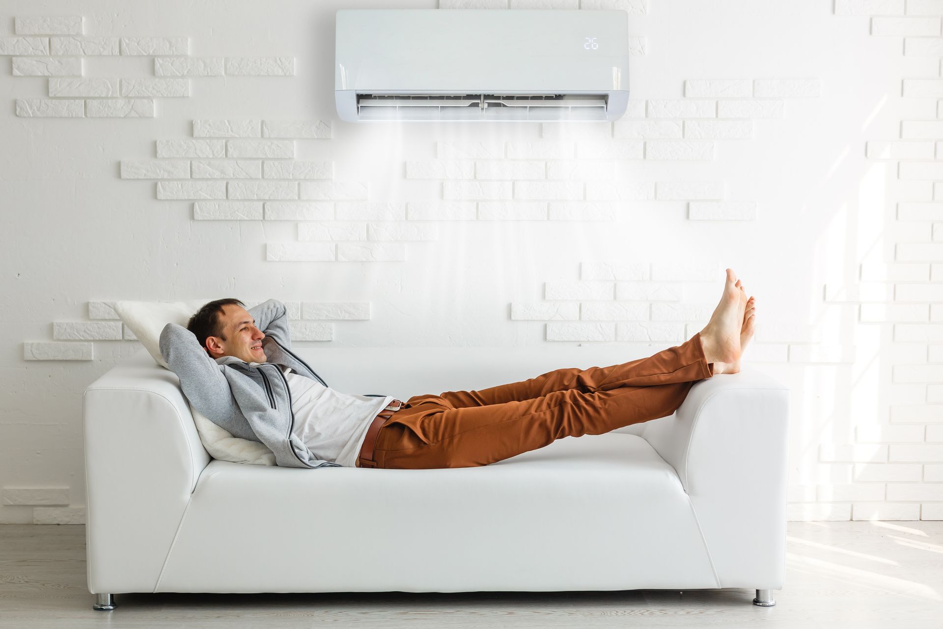 View of a man lying down and relaxing on a white sofa under an AC unit, with cool air.