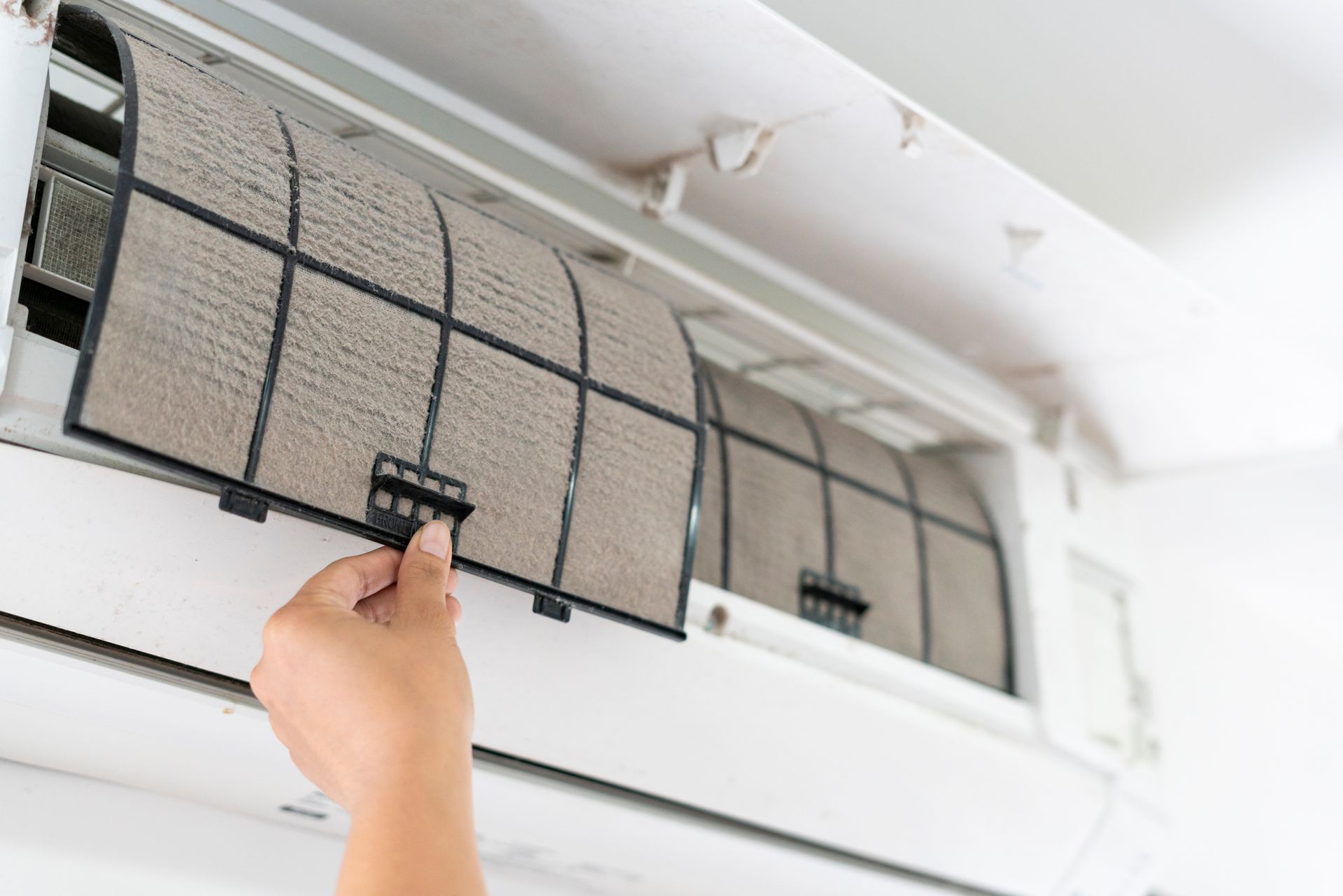 A person holds a dirty air filter while cleaning an open air conditioning unit.