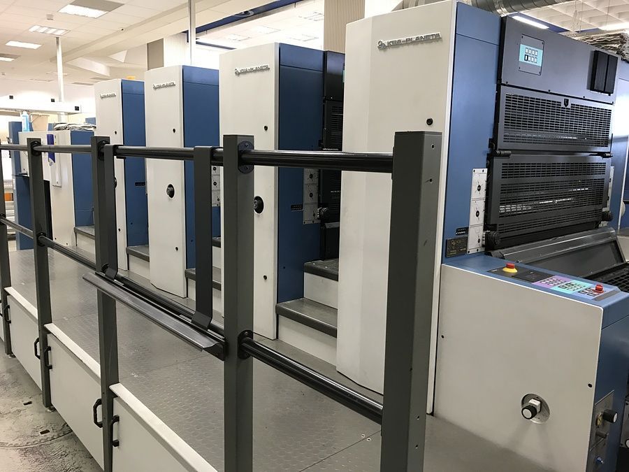 Primo piano di una macchina da stampa d'epoca con diversi rulli e componenti meccanici, in bianco e nero.