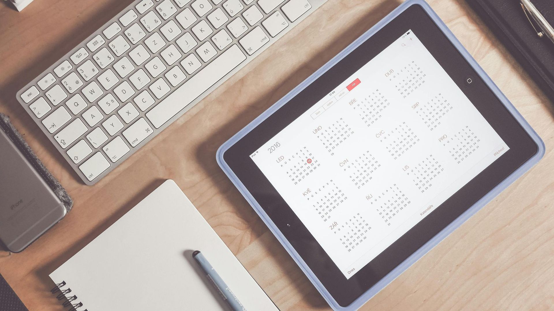 A tablet with a calendar on it is on a desk next to a keyboard.