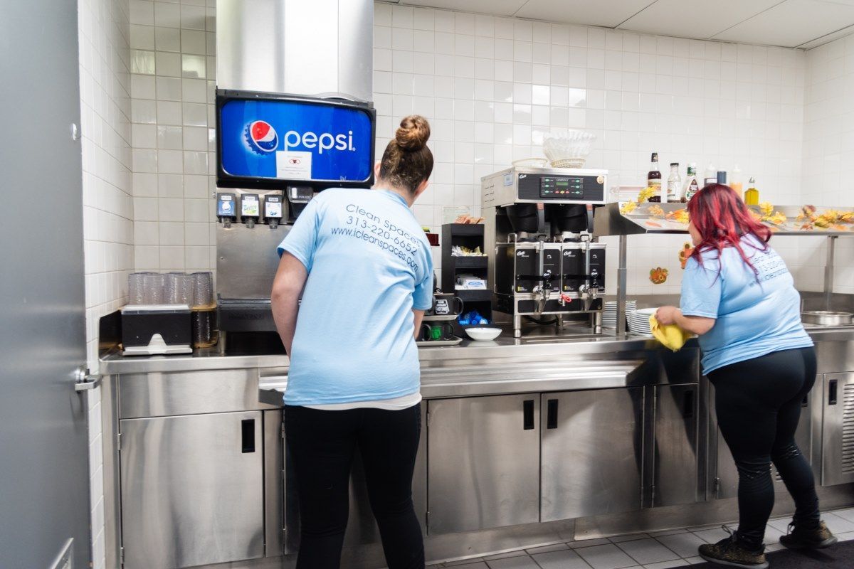 2 woman cleaning the countertops in an industrial kitchen.