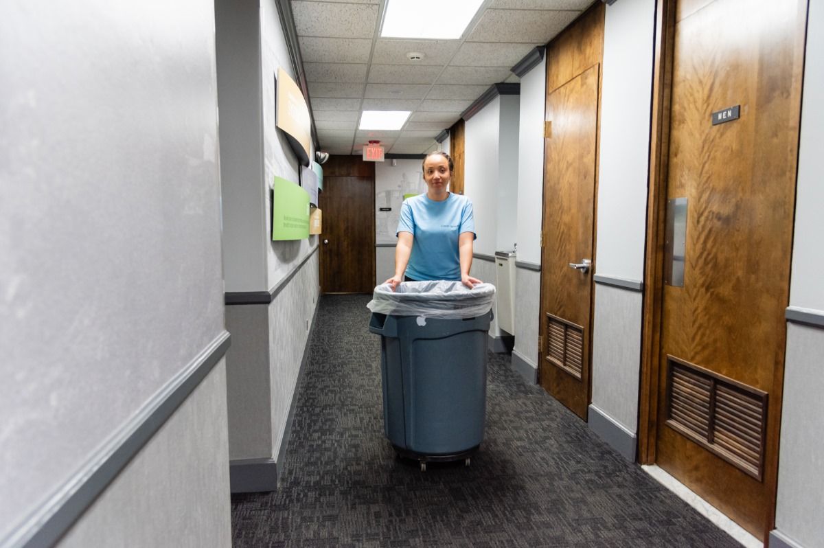Picture of a commercial cleaning girl putting away the garbage in a hallway in an office building.