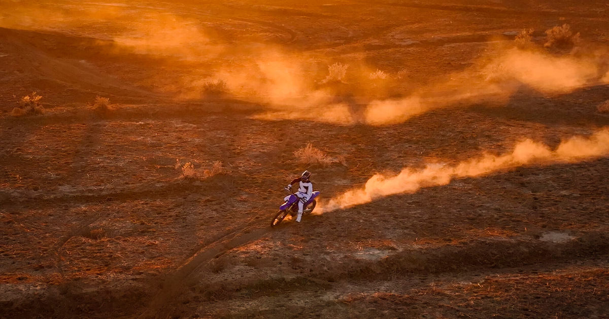Dirt bike rider racing across a dusty landscape, bathed in golden sunlight.