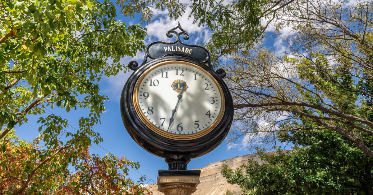 Ornate clock, black and gold, outdoors with blue sky and trees in the background.