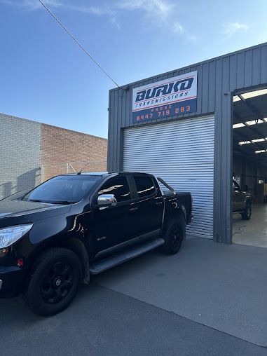 An Orange Car With the Hood Open is Parked in a Grassy Field — Burko Transmissions in Shepparton, VIC