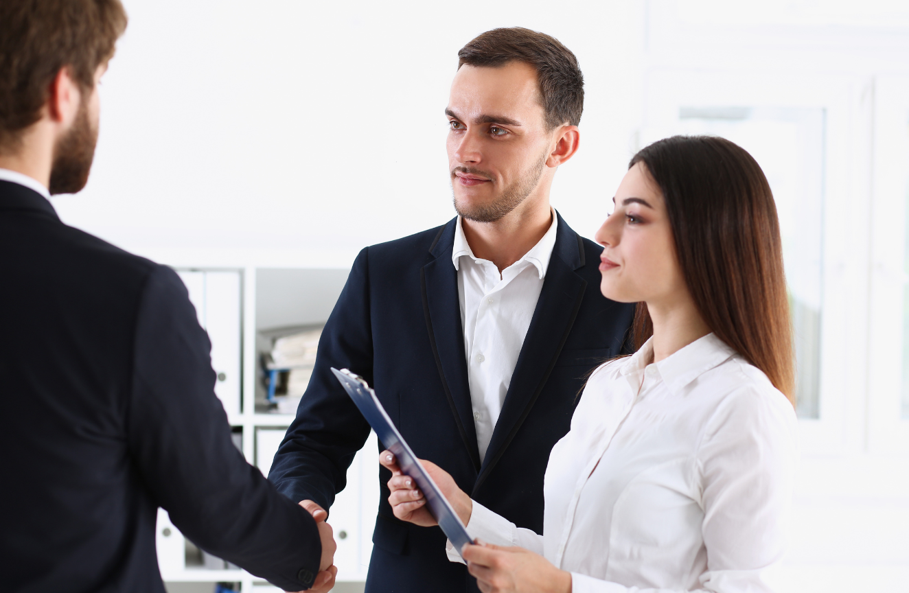 A man and a woman shaking hands with a man holding a clipboard.
