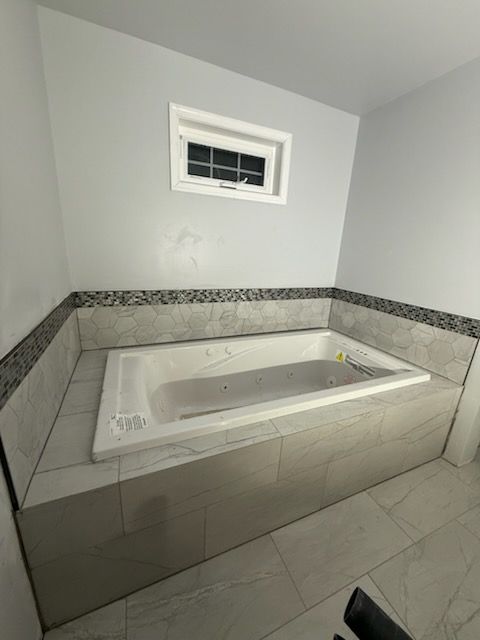 Bathroom with built-in jacuzzi tub, tiled surround, small window above. Neutral color palette.