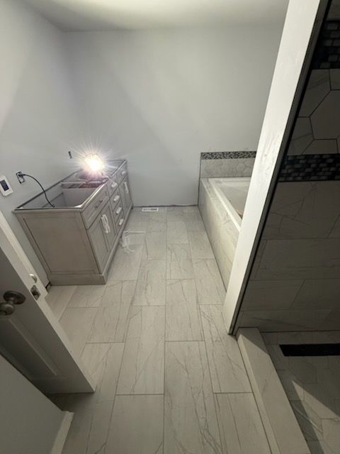Bathroom with light gray tiles and walls, vanity, and a bathtub.