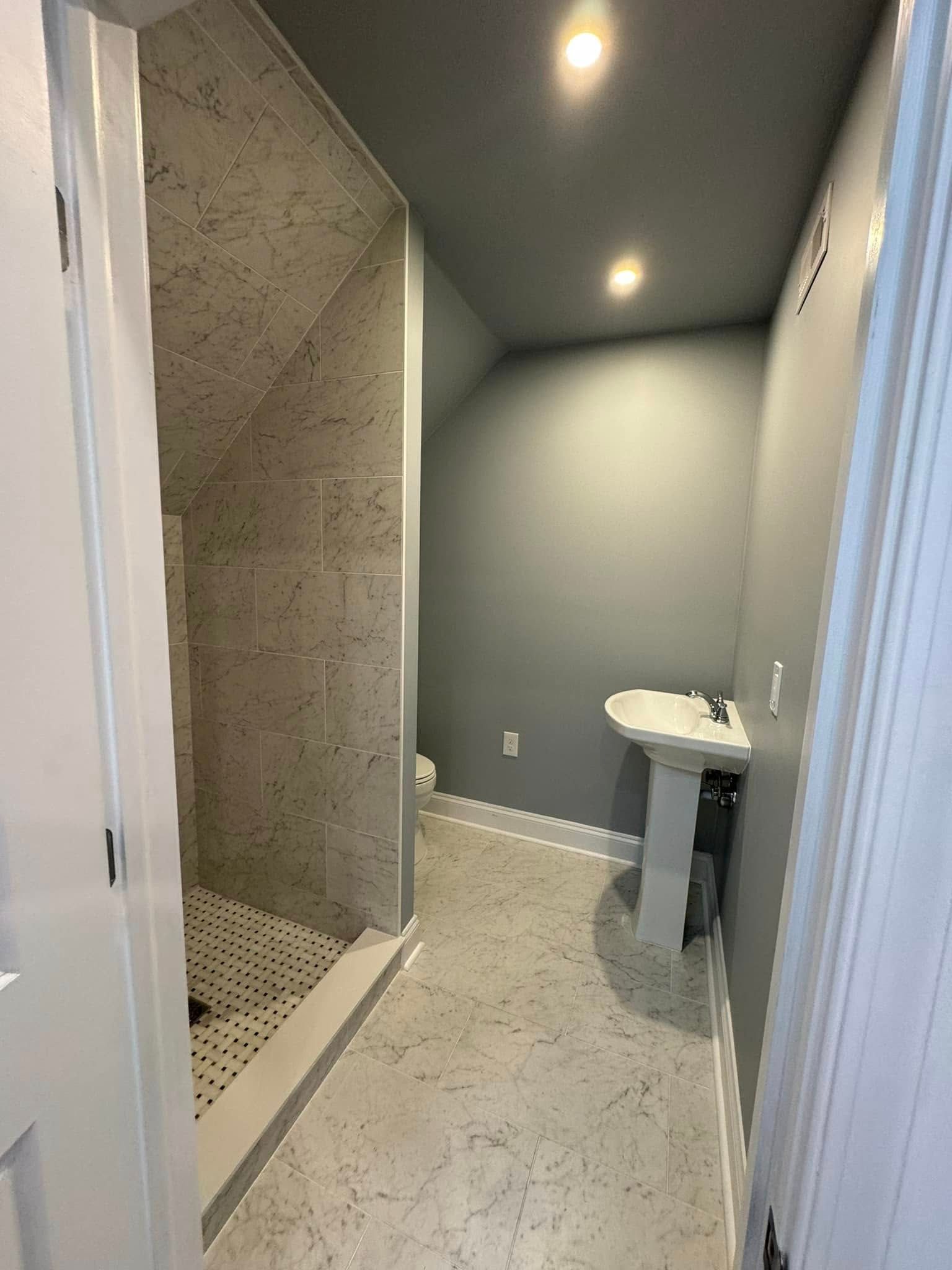 Bathroom with gray walls, speckled floor, shower, and pedestal sink.