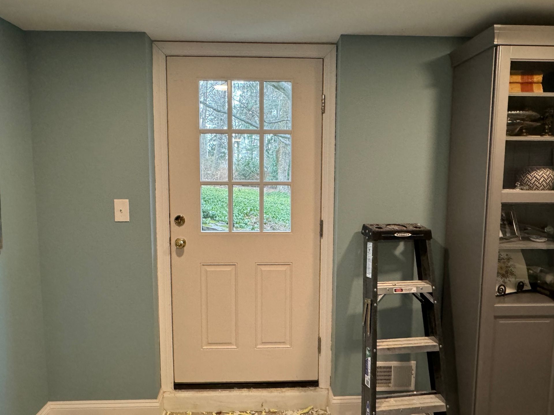 Door in a room with teal walls, a step ladder, and a cabinet.